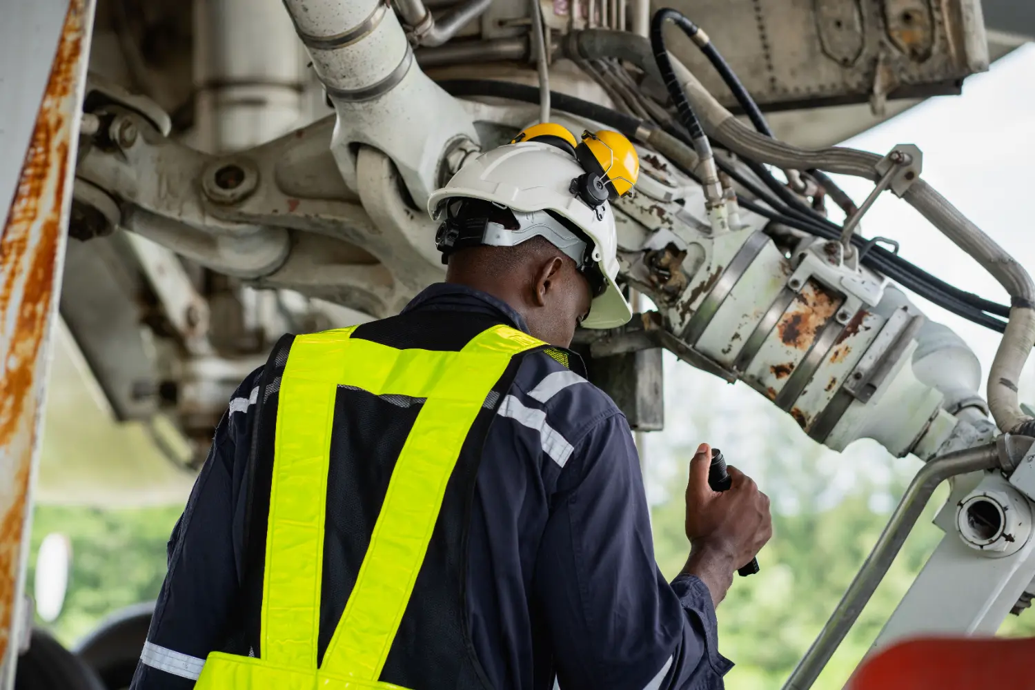Técnico inspeciona trem de pouso de avião com EPIs, focado na segurança e manutenção