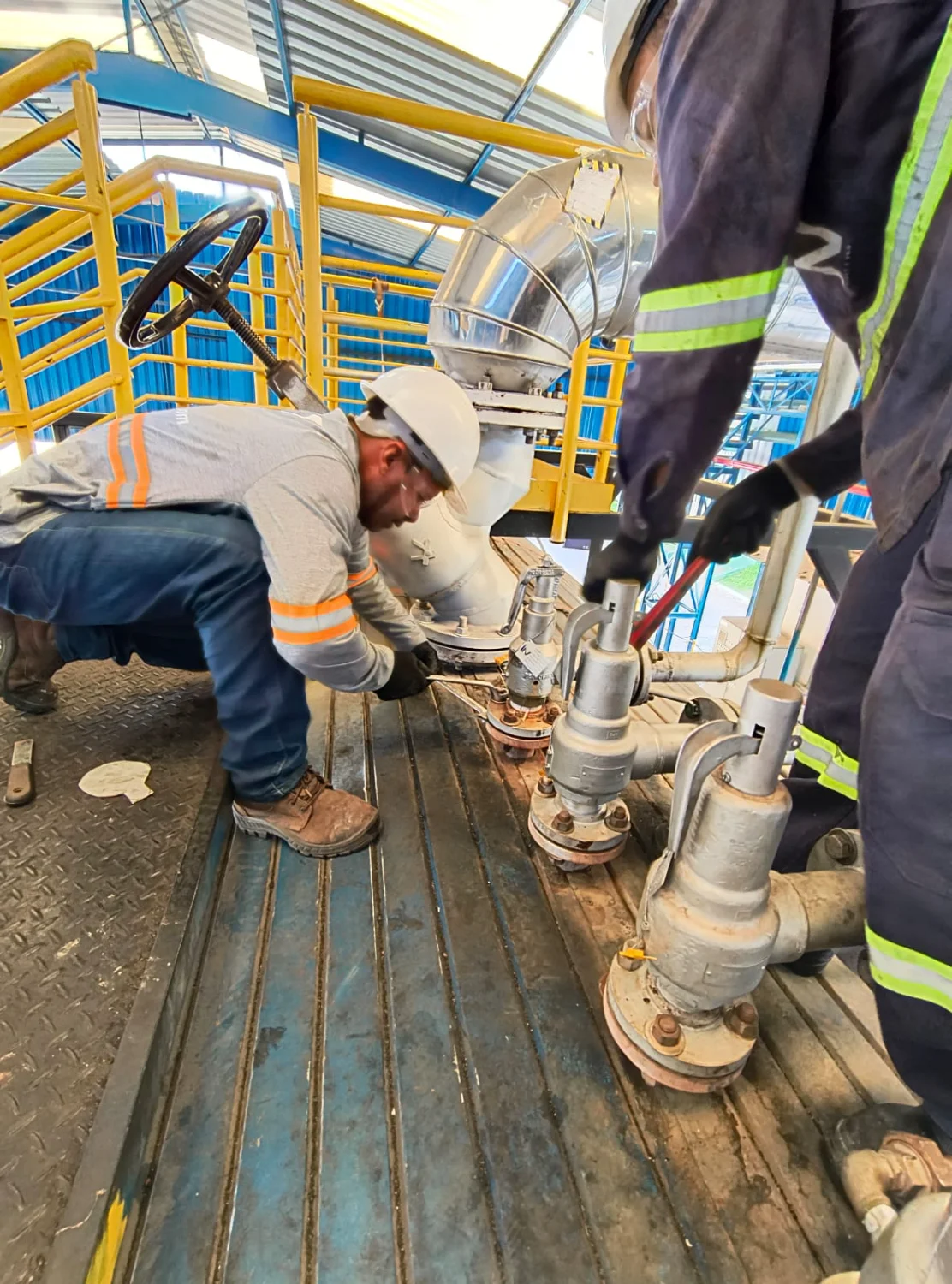 Engenheiros industriais realizando manutenção preventiva em válvulas de segurança de pressão em planta industrial, seguindo NR13.