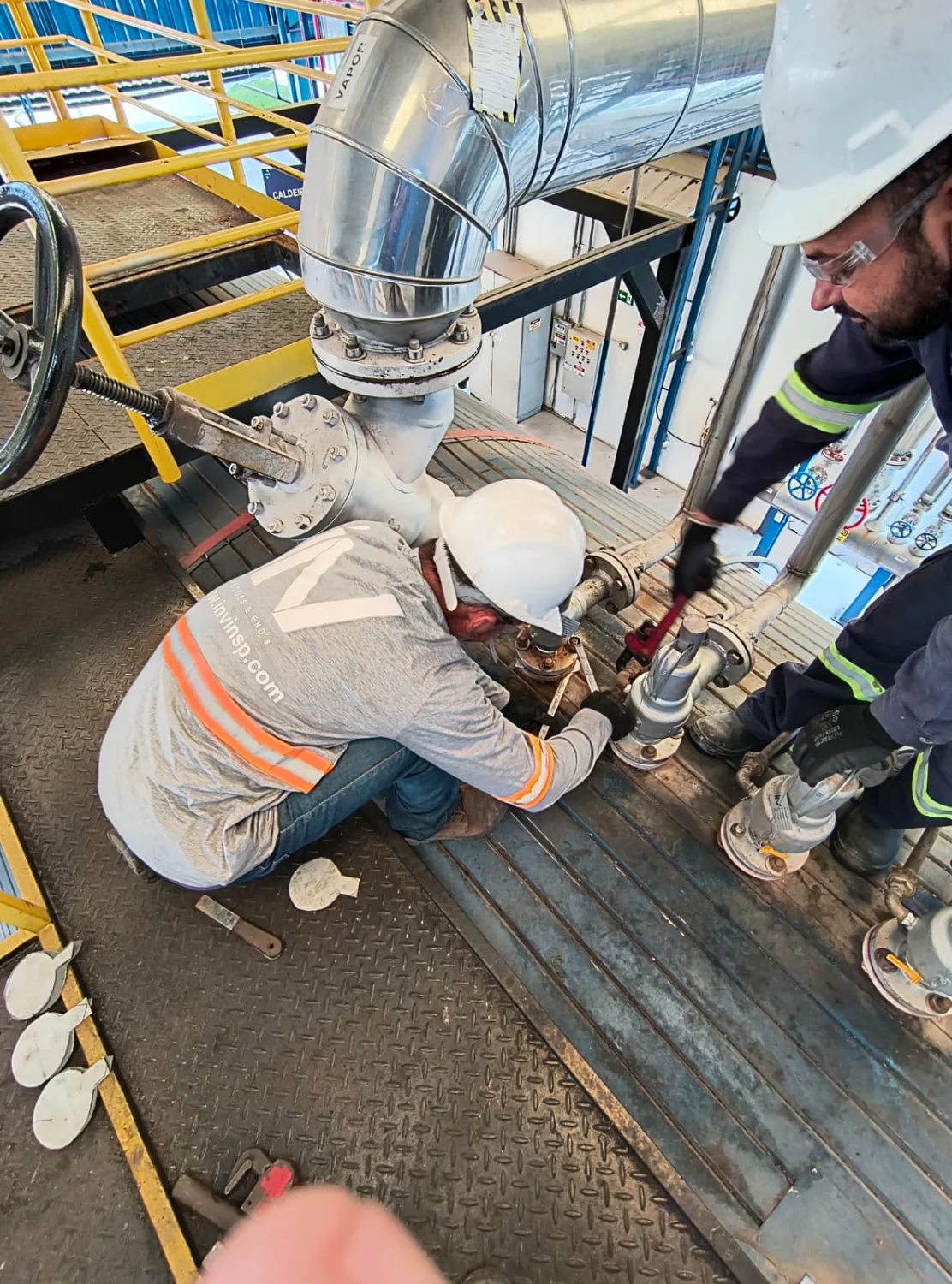 Dois técnicos qualificados inspecionam e realizam manutenção em válvulas da caldeira industrial, garantindo segurança e conformidade NR13.